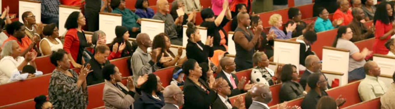A crowd of people in an African American Baptist church clapping.