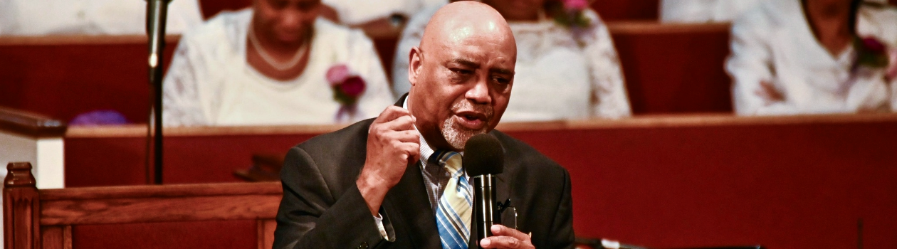 A man in a suit speaking into a microphone at Mount Olive Baptist Church in Arlington, TX.